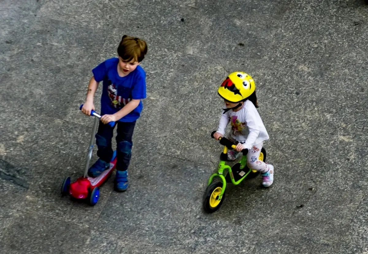 Two children riding a scooter and a balance bike seen from above